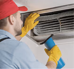A technician in gloves cleans an air conditioning duct using a brush.