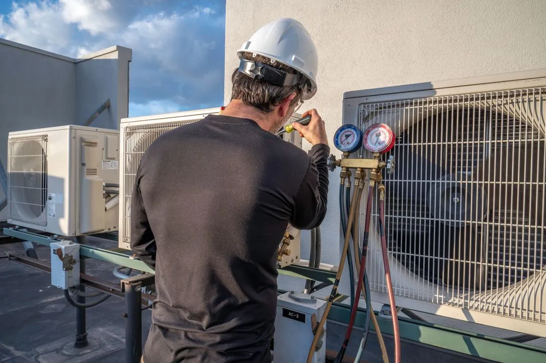 A technician inspects air conditioning units on a rooftop using gauges and tools for maintenance.